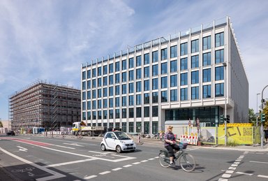 Bauteil 1 während der Fertigstellung im städtischen Kontext: Der klare Kubus fügt sich selbstbewusst in die Umgebung ein und definiert den Straßenraum neu. - © caspar./HGEsch